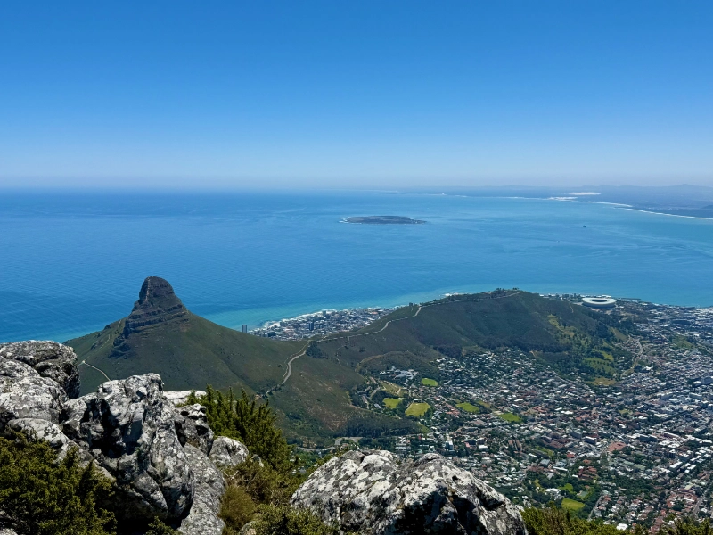 Blick vom Tafelberg auf den Lion's Head (links) und den langgestreckten Bergrücken Signal Hill. Die Insel im Atlantik ist Robben Island.